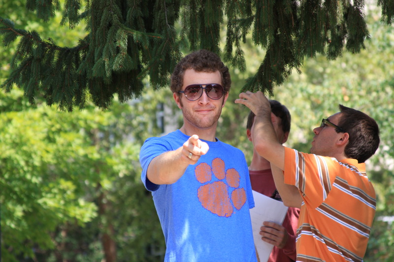 A man wearing sunglasses and a Clemson t-shirt points at the camera