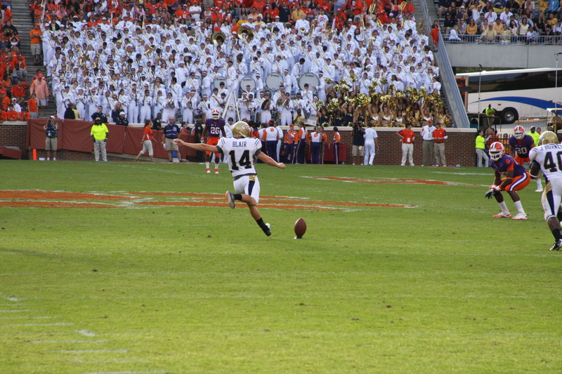 A football kicker swings, about to make contact with the football at kickoff