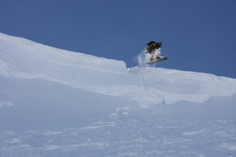 A snowboarder takes to the air off a snowy cliff